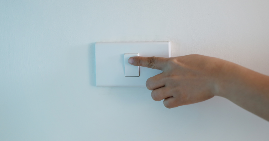 tips to warm your home - person turning off light switch with their hand